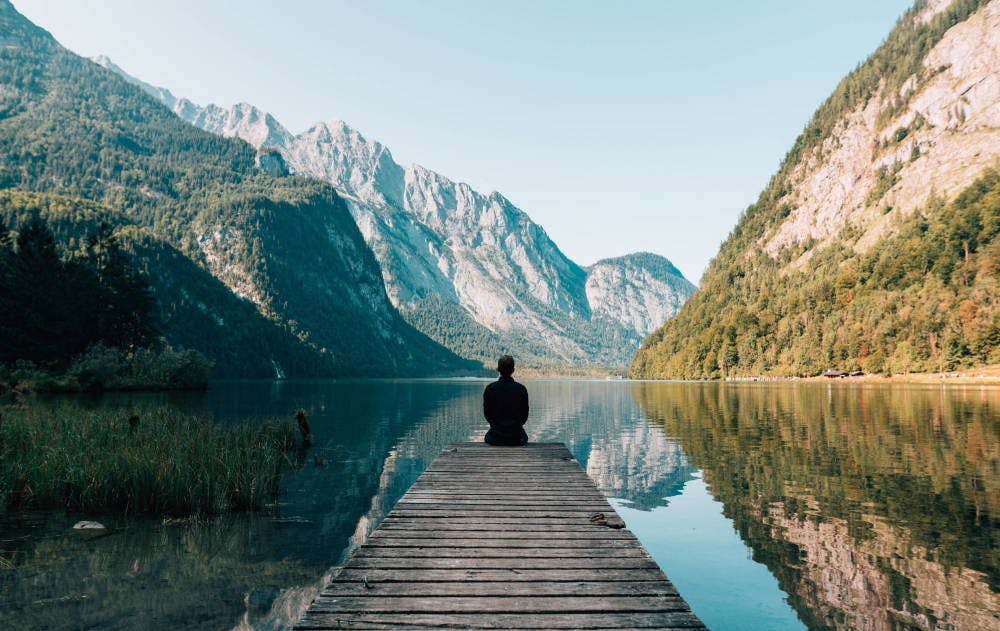 Someone sitting on the end of a pier looking out at mountains